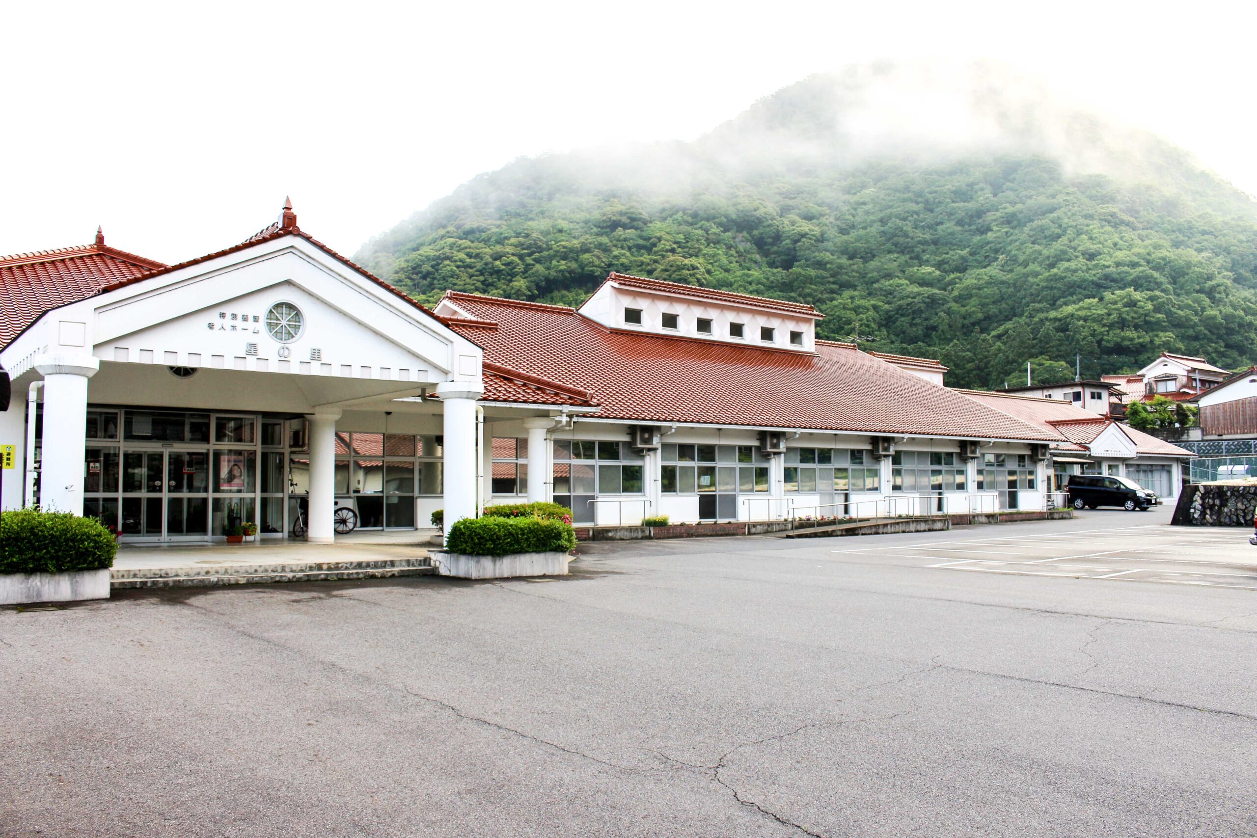 山麓に建つ介護施設の建物全景。白壁と赤瓦屋根の平屋造り。